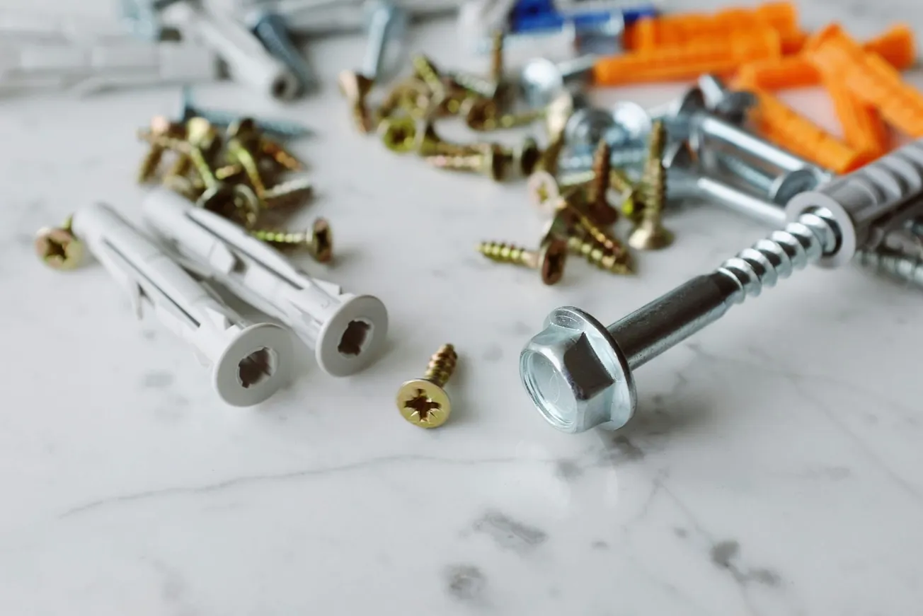 Scattered screws, bolts, and wall plugs on a white marble surface, conveying a sense of DIY or home improvement readiness and potential creativity.