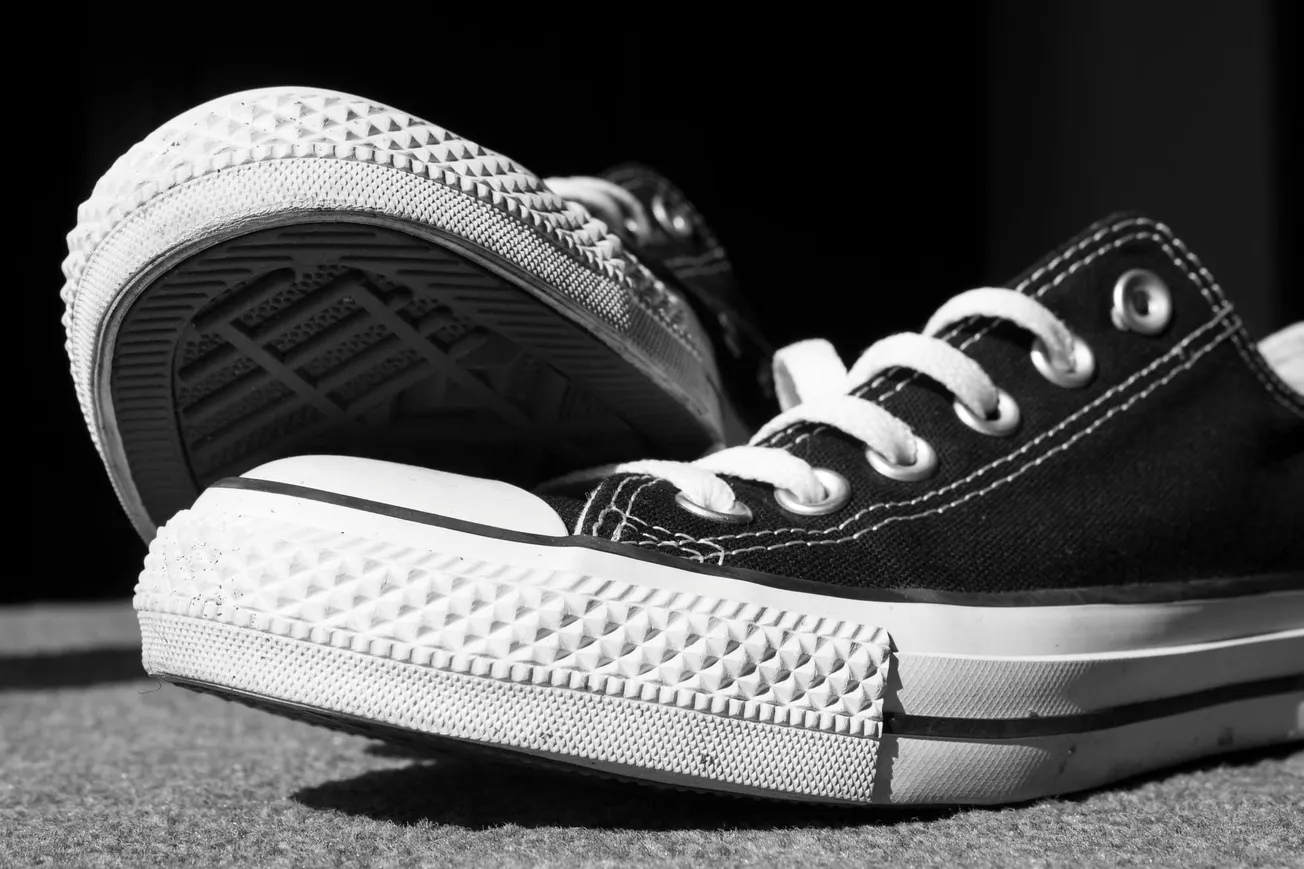 Black and white close-up of classic canvas sneakers on a textured surface. The focus is on the detailed rubber sole and white laces, conveying a casual vibe.