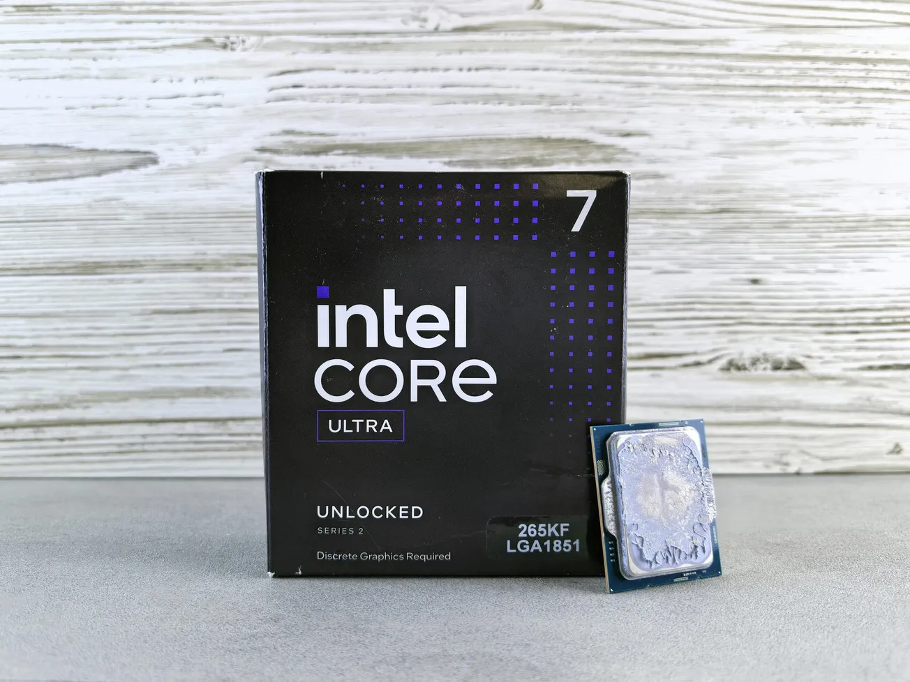 Box of Intel Core Ultra 7 Processor with model 265KF LGA1851, placed on a wooden background. The processor is displayed alongside the box.
