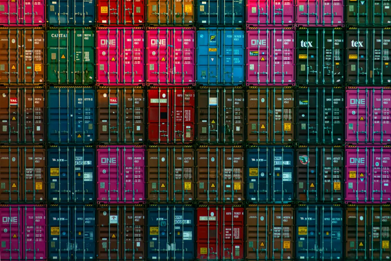 A stacked wall of colorful shipping containers, features rows of blue, red, green, pink, and brown units. The scene conveys industrial order.