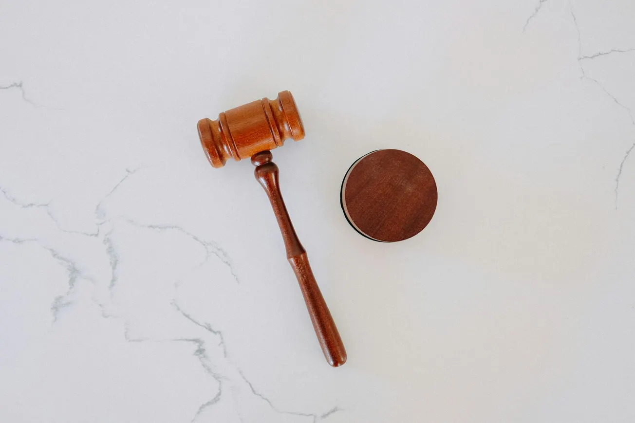 Wooden judge's gavel resting beside a round sound block on a white marble surface, evoking themes of justice and authority.