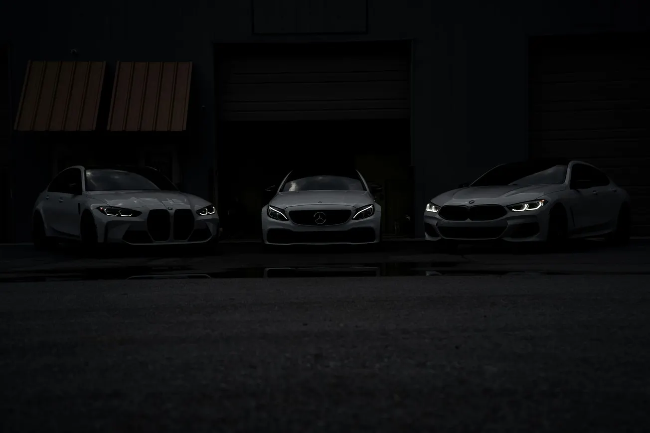 Three luxury cars with headlights on are parked in a dark garage. The dim lighting creates a mysterious and sleek atmosphere.