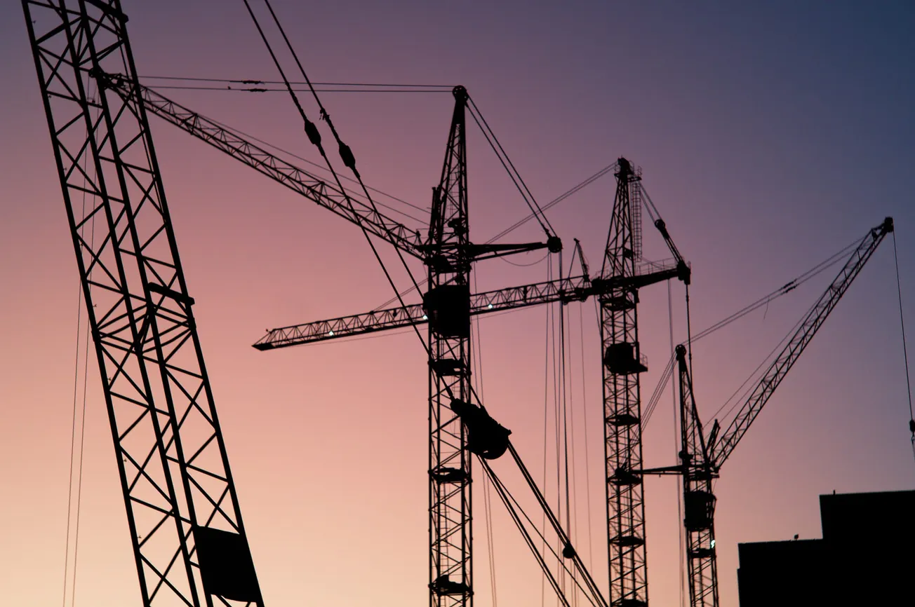 Silhouetted construction cranes against a serene, purple-orange twilight sky, conveying a sense of progress and industrial development.
