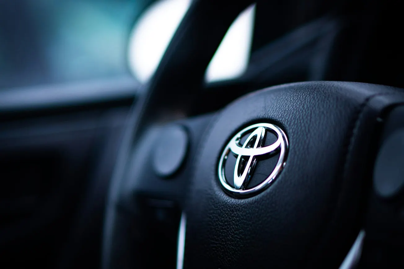 Close-up of a car steering wheel featuring the Toyota logo in shiny chrome on black leather, conveying a sleek and modern automotive feel.