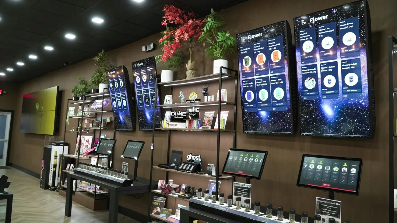 Modern cannabis dispensary interior with digital menus showcasing products, sleek wooden shelves displaying various items, and ambient lighting.