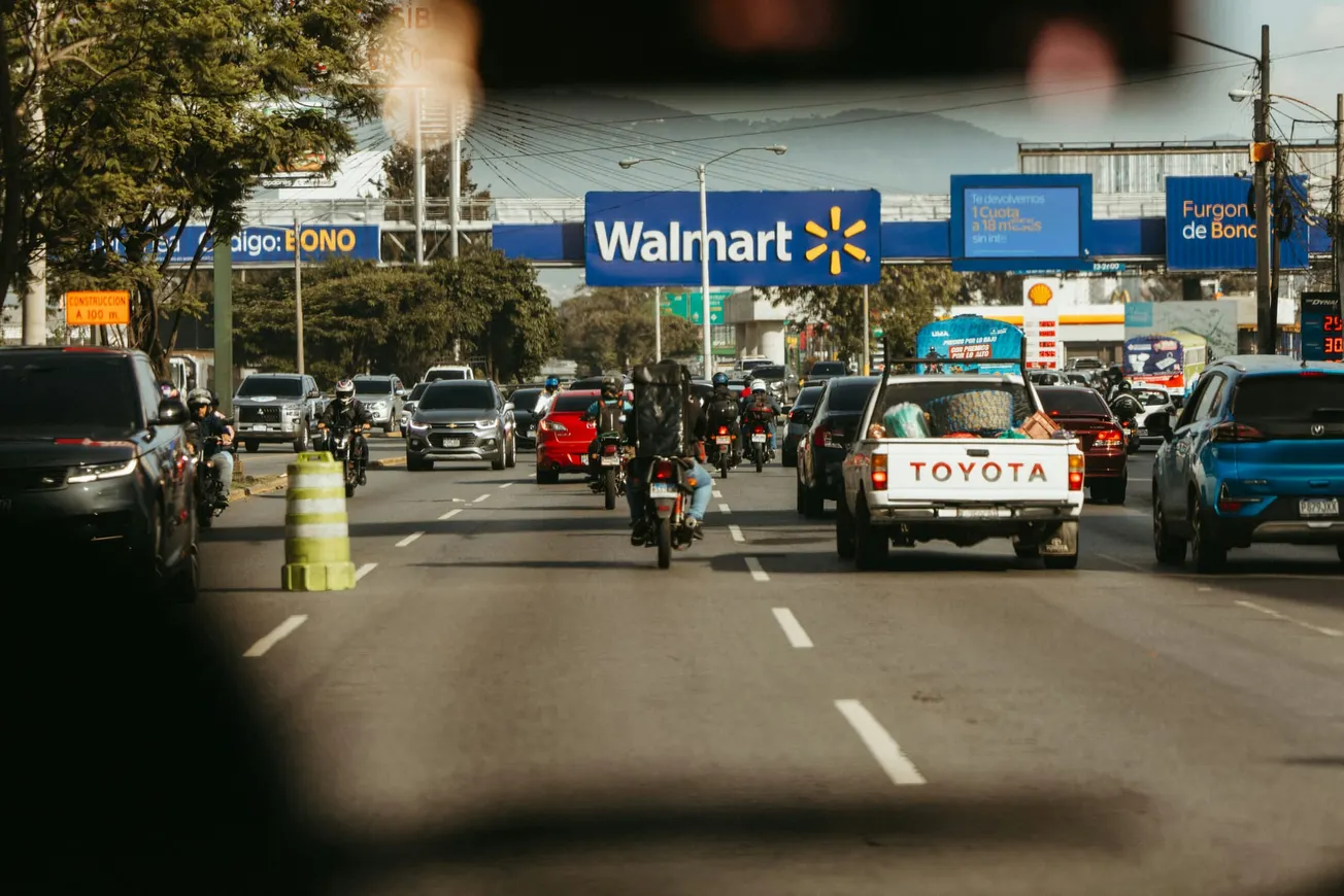 Traffic on a busy street with cars and motorcycles, leading to a Walmart sign. The scene conveys a bustling urban atmosphere.