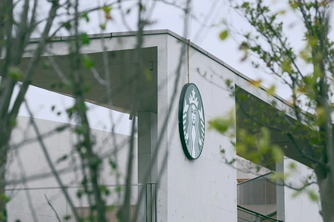 Modern concrete building with Starbucks logo, seen through blurry branches, conveying a minimalist and natural urban atmosphere.