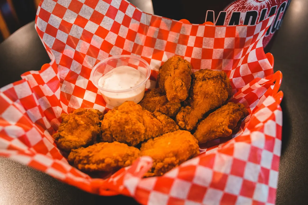 Basket of crispy fried chicken wings on red checkered paper, with a side of creamy dipping sauce. Warm, inviting, and deliciously appetizing.