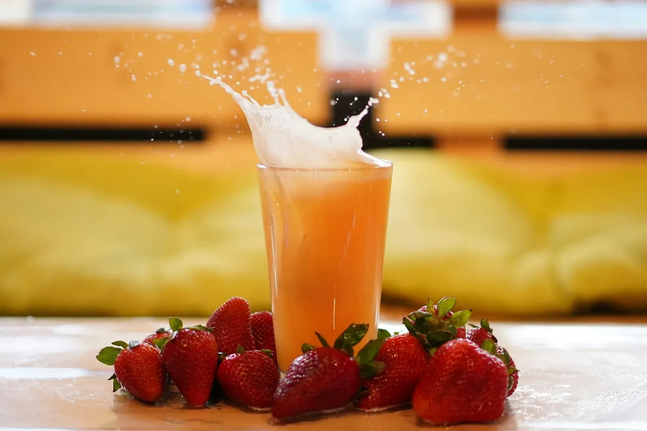 A refreshing splash erupts from a glass of orange juice surrounded by ripe strawberries on a wooden table, conveying freshness and vitality.