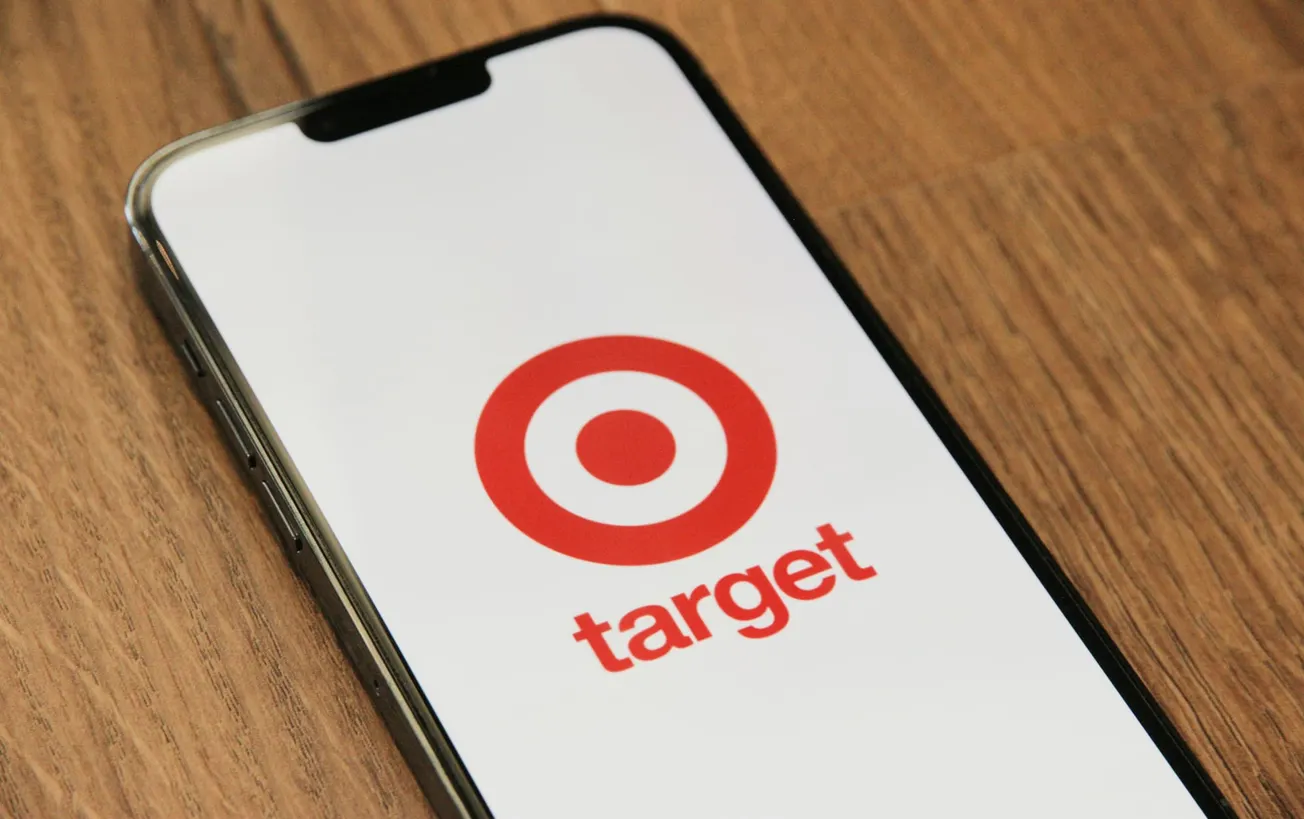 Smartphone displaying the Target logo with a red bullseye and the word "target" on a white screen, placed on a wooden surface.