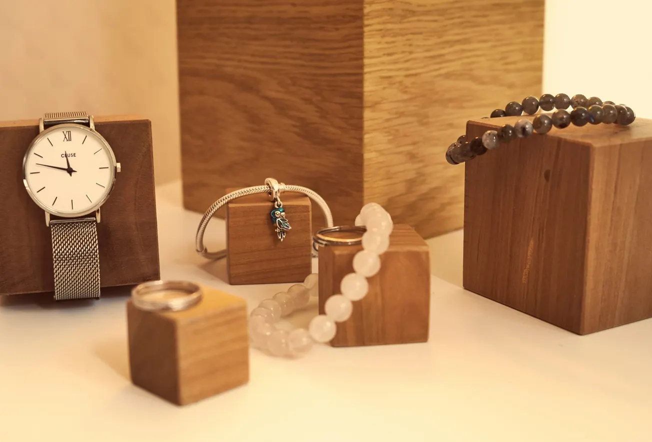 Stylish watch and various bracelets displayed on wooden blocks. The scene conveys elegance and warmth, with a focus on texture and neutral tones.