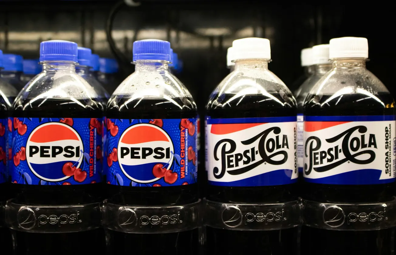 Close-up of two Pepsi bottles, one with a wild cherry label in blue and red, the other with a retro Pepsi-Cola design. A cheerful, nostalgic vibe.