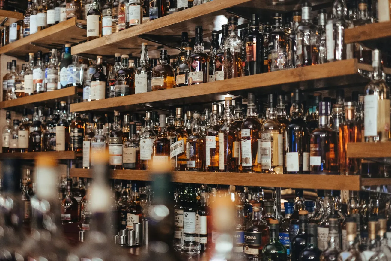 Shelves filled with assorted liquor bottles, mostly whiskey, create a cozy bar atmosphere. The warm lighting enhances the inviting, rich tones.