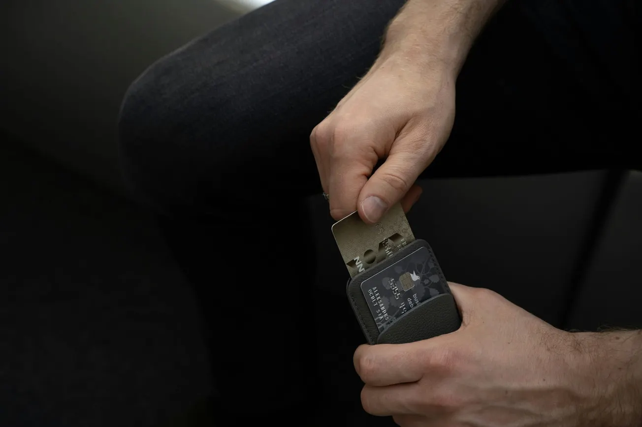 A person inserts a gray metal card into a handheld sharpening tool, demonstrating a precise task. The lighting is subdued, creating a focused mood.