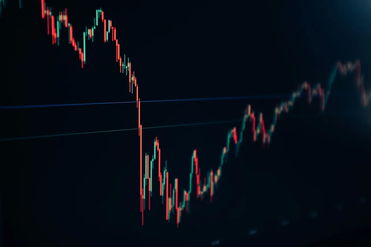 A dark financial chart displays a steep red downtrend line with consecutive peaks and troughs, conveying a sense of market volatility and decline.