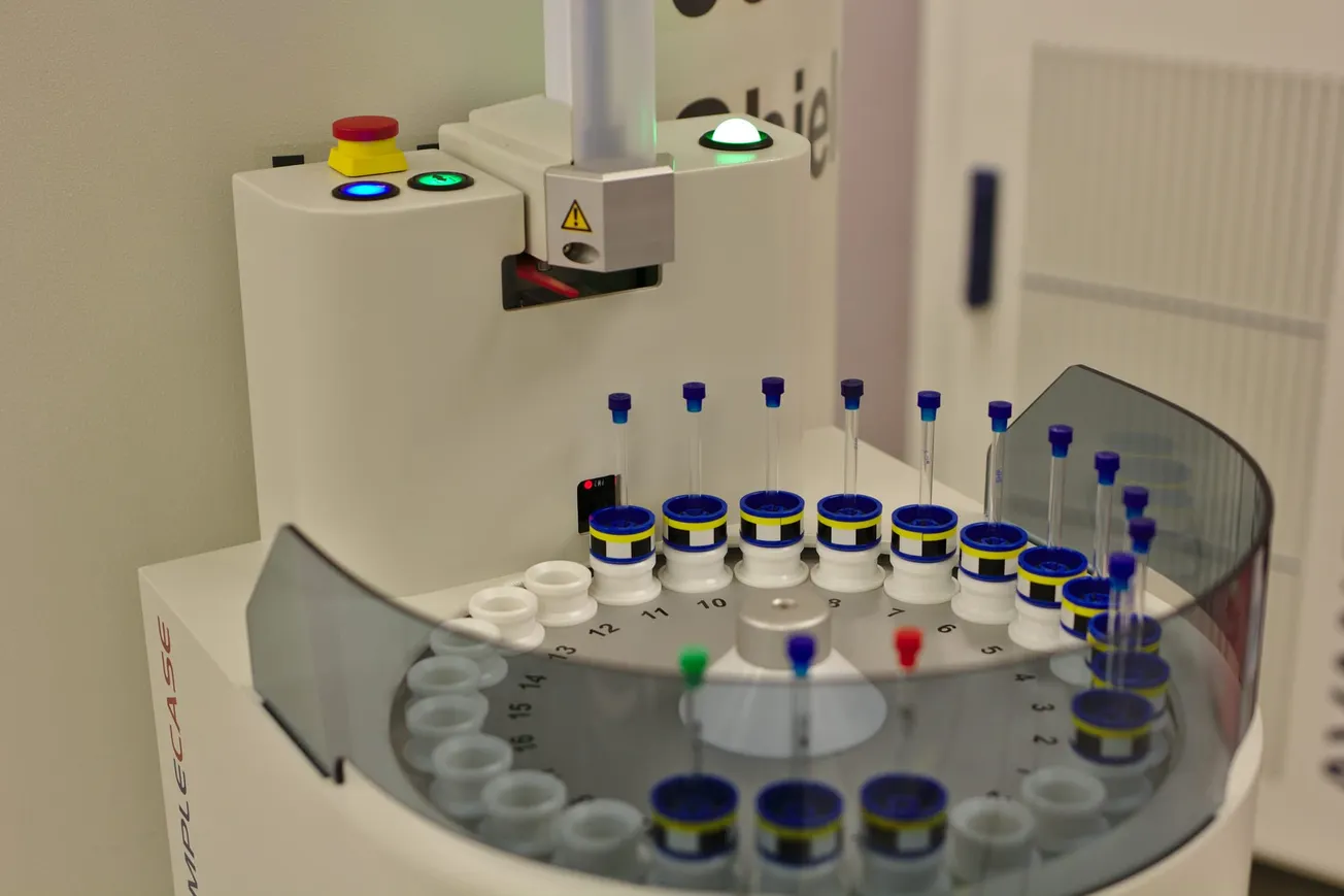 A close-up of a laboratory centrifuge with numbered slots holding test tubes with blue caps. The device displays buttons and lights on top, conveying a high-tech and precise environment.