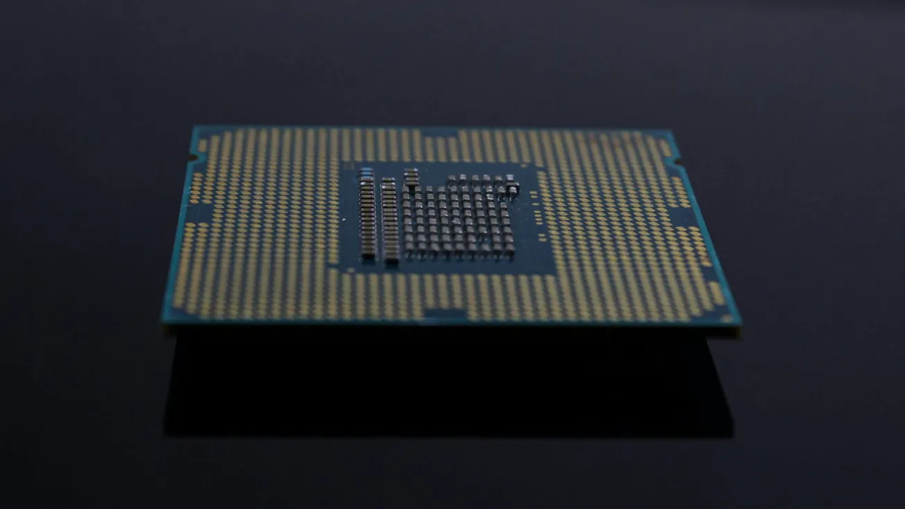 Alt text: Close-up of a computer microchip with a grid of metallic pins on a blue-green surface, set against a sleek black background.