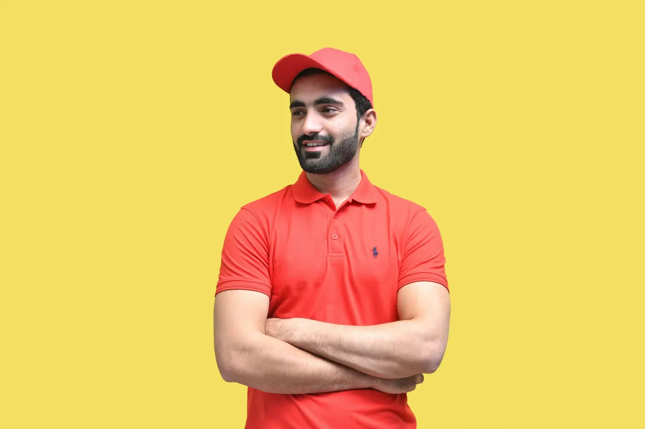 Man in a red polo shirt and cap with folded arms smiles against a bright yellow background. The tone is casual and cheerful.