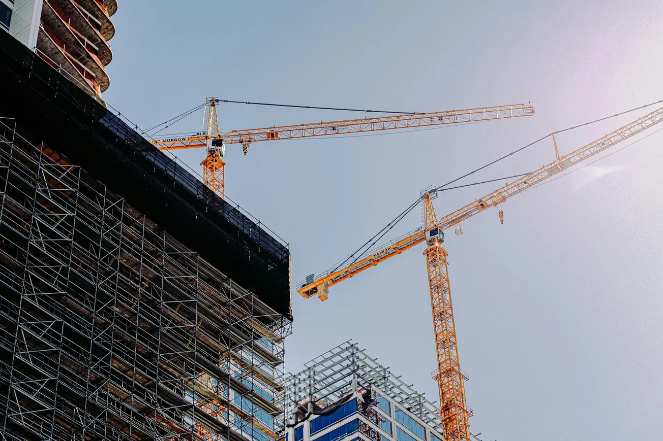 Two towering cranes loom over the construction of tall buildings against a clear blue sky, embodying progress and urban development.