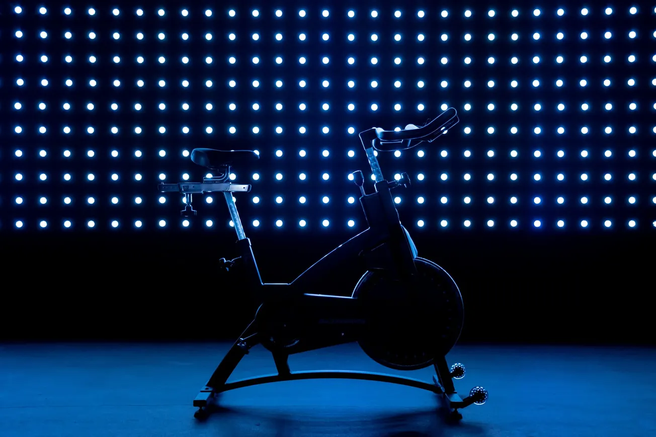 Silhouetted exercise bike with a modern design is highlighted against a grid of glowing blue LED lights, creating a futuristic and energetic atmosphere.