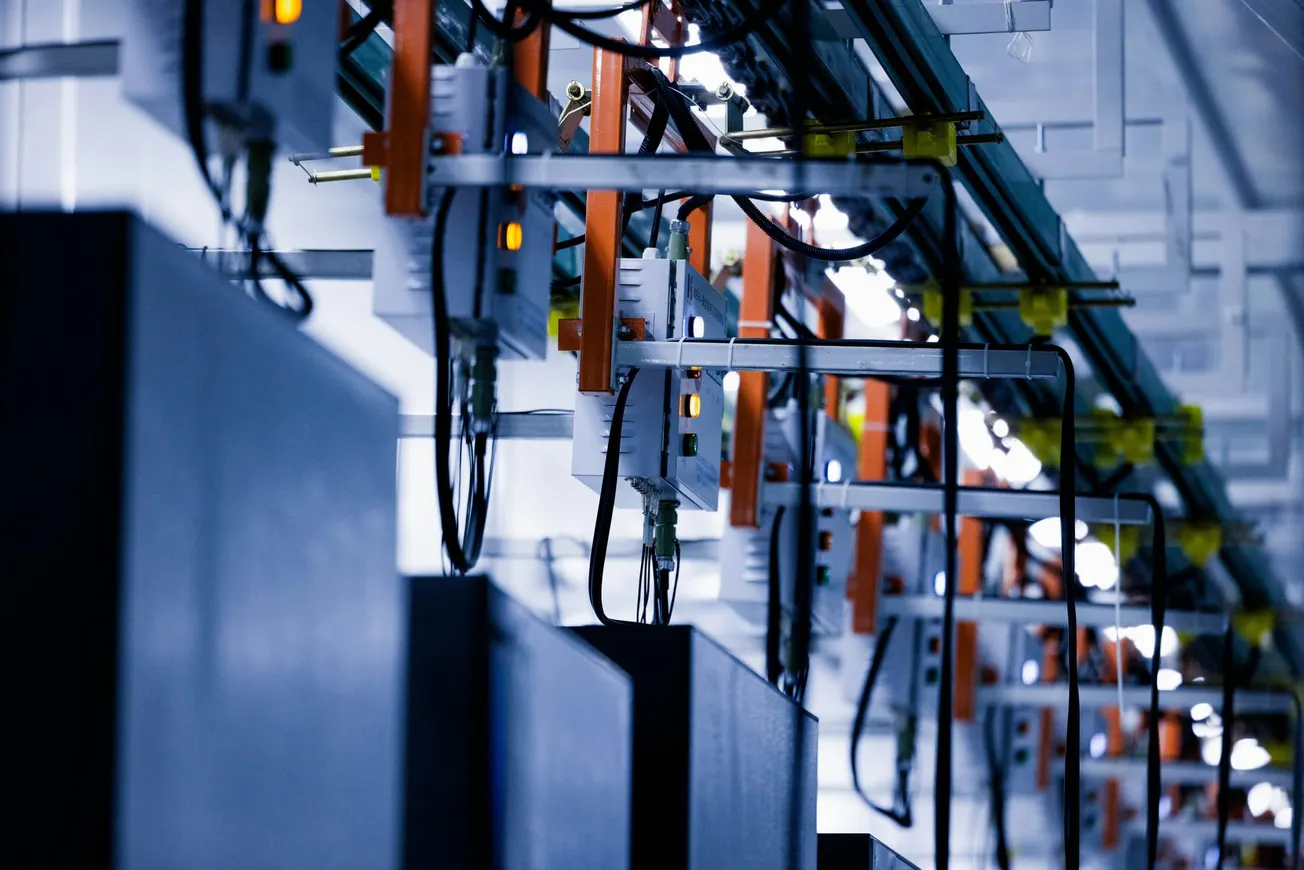 Rows of industrial electrical wiring and circuits with orange connectors and cables, set in a dimly lit, modern technological facility.
