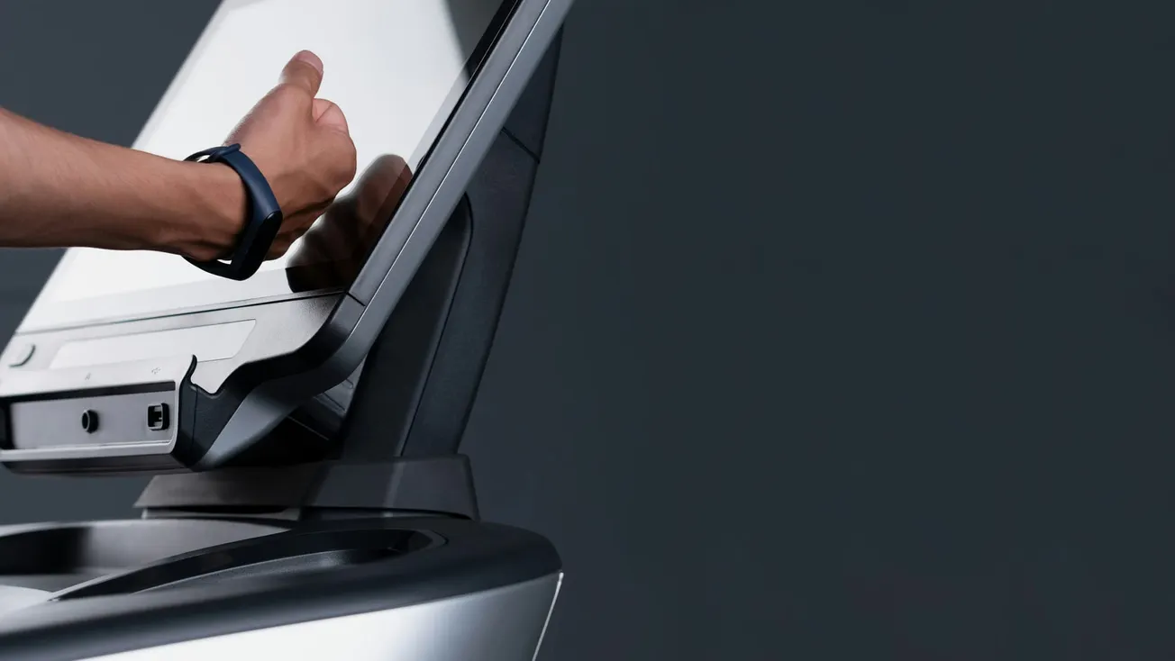 A hand wearing a smartwatch operates a sleek touchscreen device against a dark background, conveying a sense of modern technology and interaction.