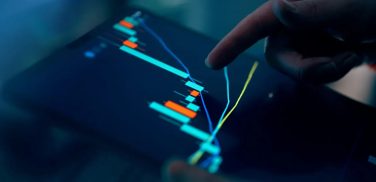 Close-up of a hand pointing at a digital tablet displaying a dynamic stock market chart with colorful candlesticks and trend lines, conveying analysis.