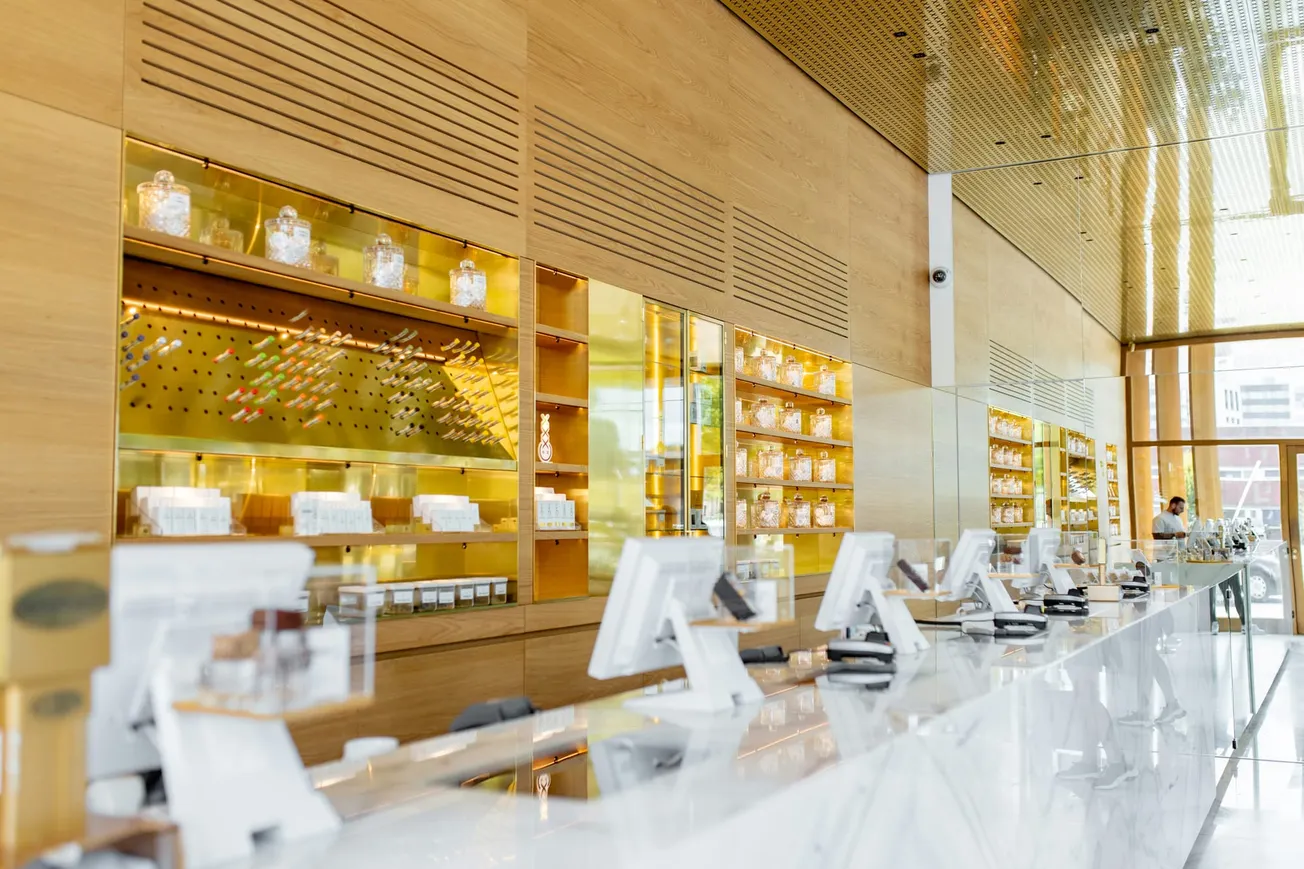 Bright, modern dispensary interior with sleek white counters, touchscreen devices, and illuminated shelves displaying products in glass jars.