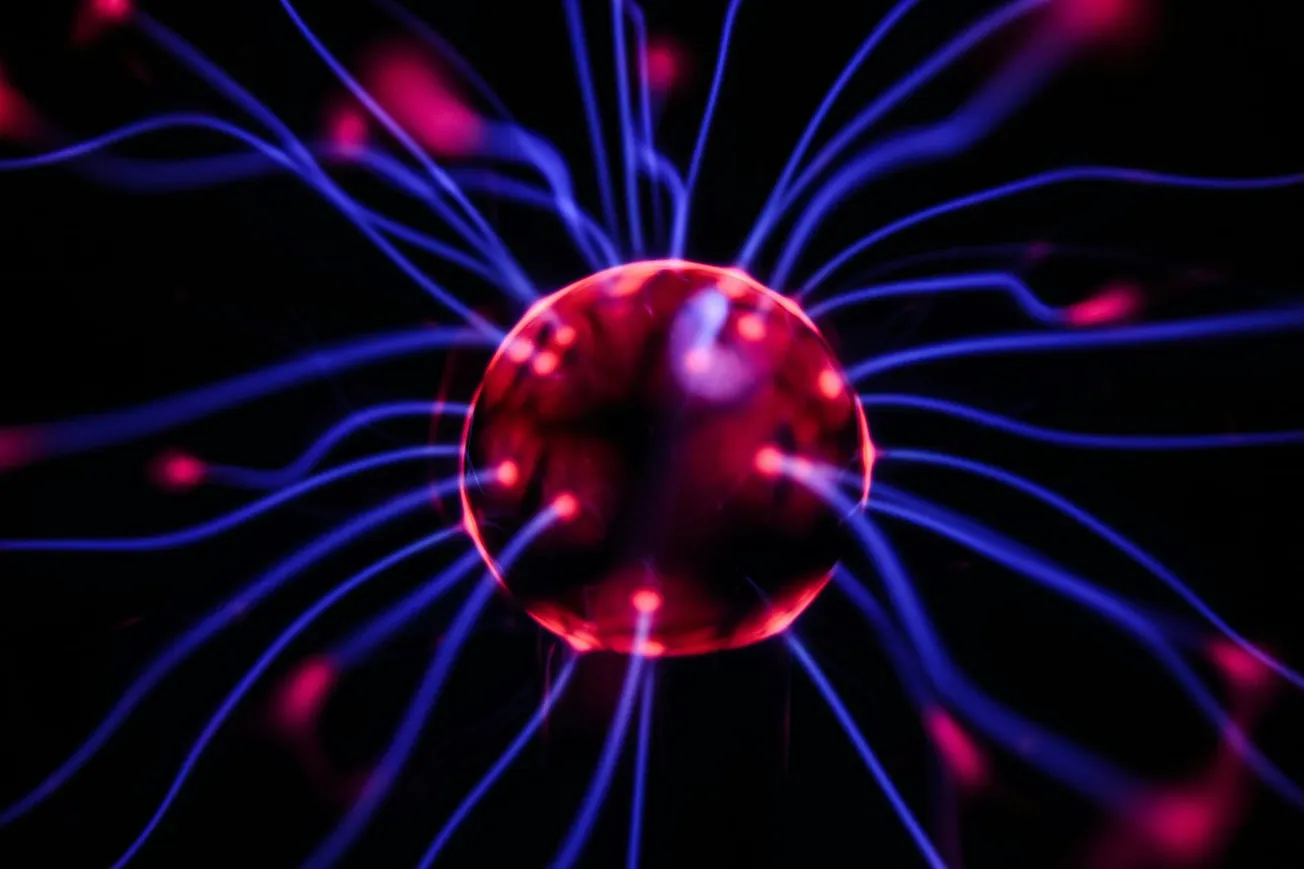 A vibrant plasma globe emits glowing blue and pink strands of light from a central sphere against a dark background, creating an energetic and dynamic effect.