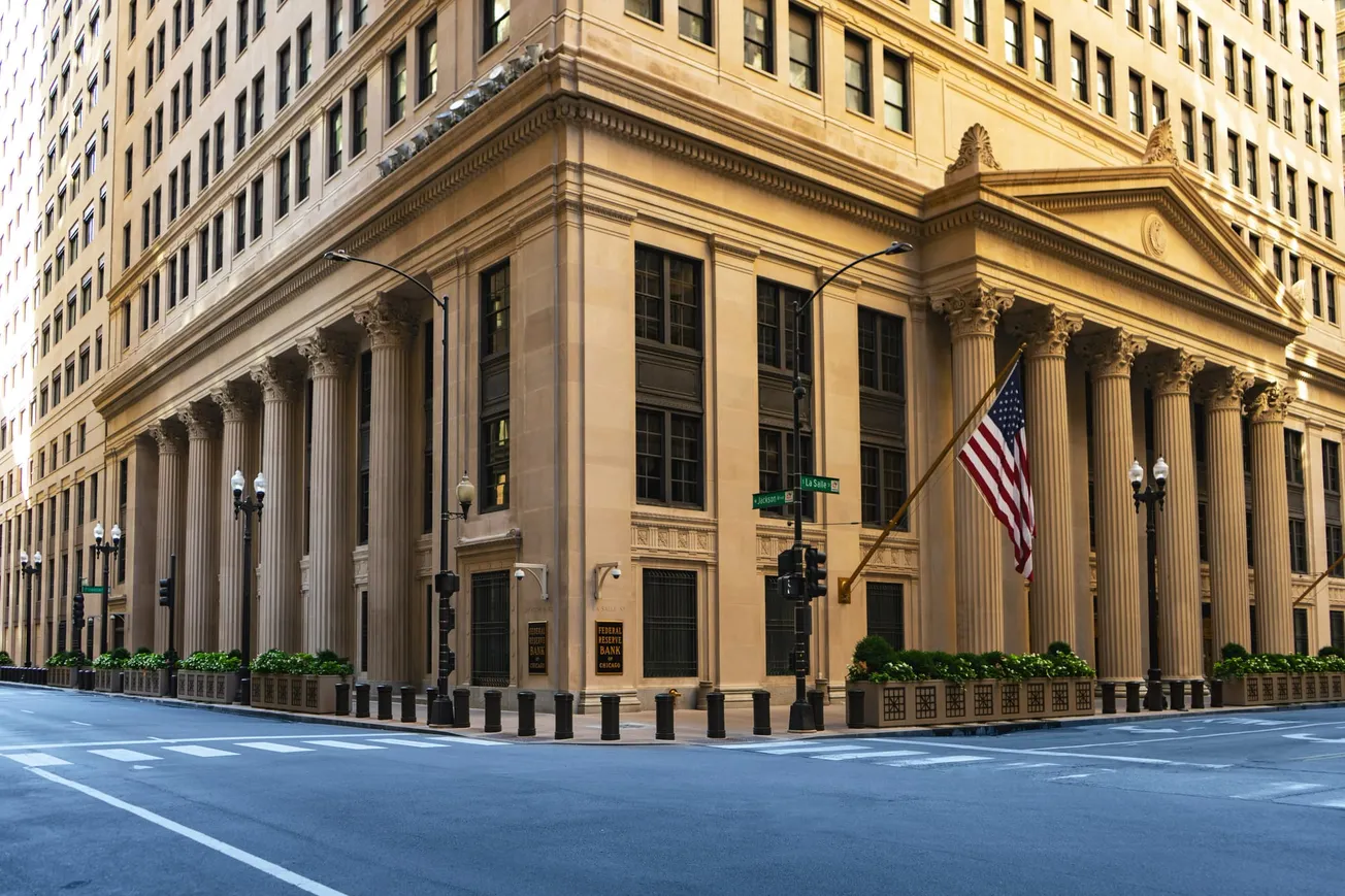 Historic building with tall columns on a street corner. An American flag hangs prominently. The scene conveys a sense of grandeur and stability.