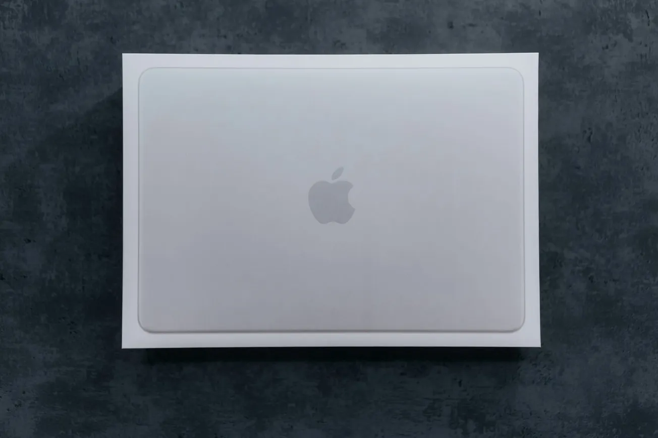 Closed, white laptop box on a dark, textured surface. The laptop features an apple logo, creating a minimal and sleek design.