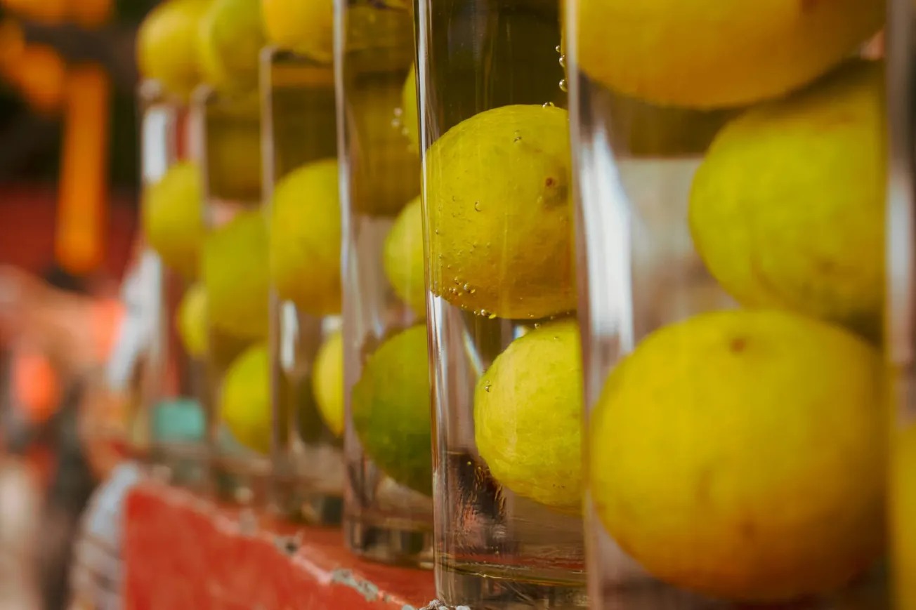 Rows of lemons submerged in glass jars filled with clear water, creating a vibrant and refreshing display on a red surface background.