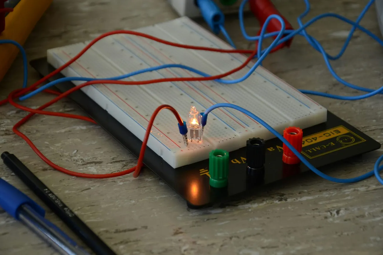 Close-up of a breadboard with colored wires and a glowing LED, set on a textured surface, conveying a sense of hands-on experimentation.