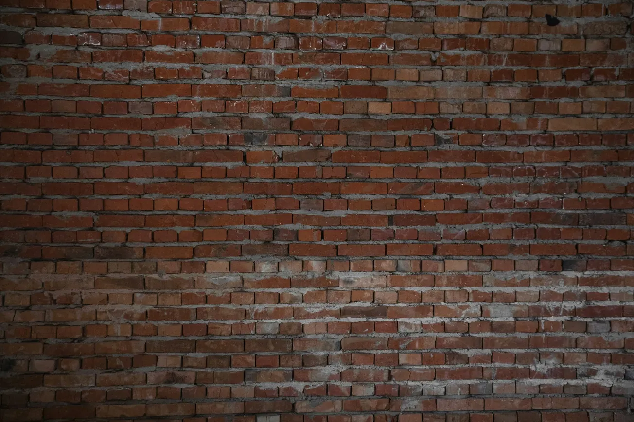 A textured red brick wall with unevenly applied gray mortar. The lighting is soft, creating a rustic and industrial feel.