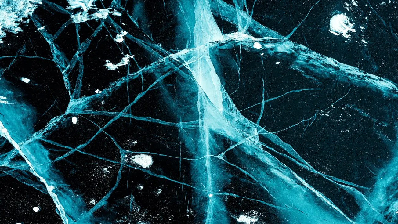 Abstract image of cracked blue ice with intersecting lines and textures. It conveys a cold, dynamic atmosphere with bright highlights and deep shadows.
