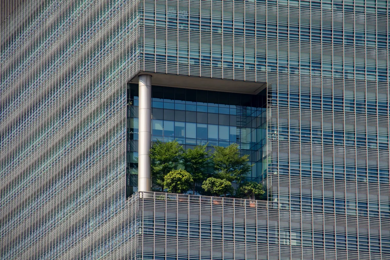 A close-up of a modern building facade with a large, rectangular inset balcony showcasing green trees. The facade's grid pattern gives a sleek, contemporary feel.