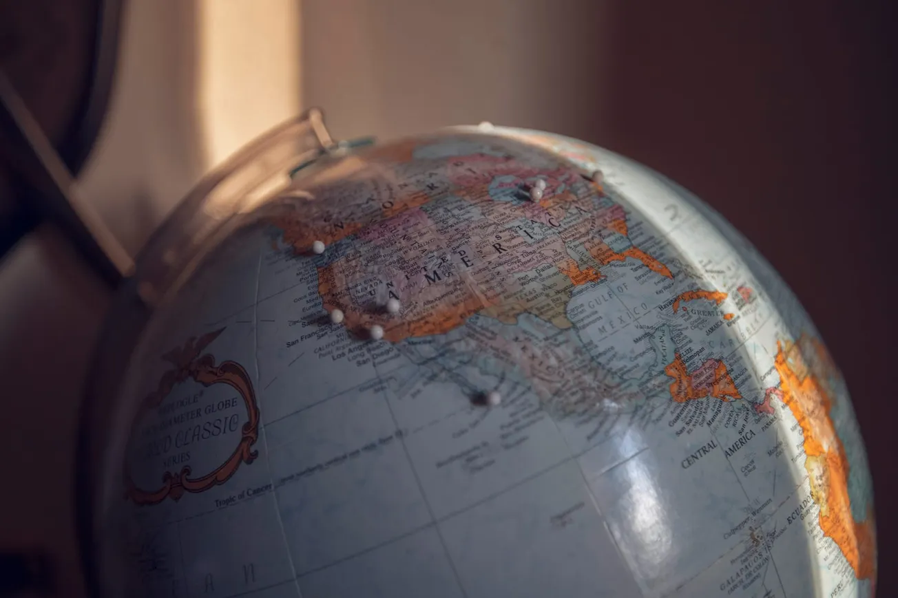 Close-up of a vintage globe in soft light showing North America. The atmosphere is warm and nostalgic, with detailed maps and muted colors.