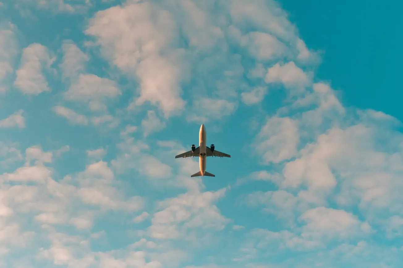 Airplane flying through a partly cloudy sky. The plane is centered, contrasting with the blue sky, evoking a sense of travel and freedom.
