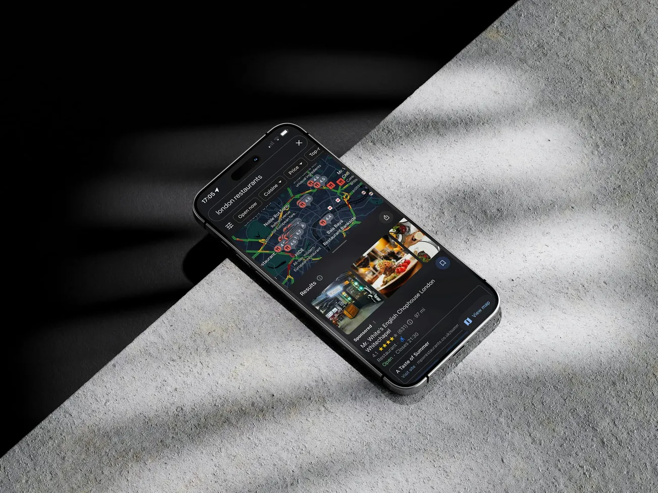 A smartphone displaying a dark-themed map app with location pins lies on a shaded, textured surface. The mood is sleek and modern, suggesting travel or navigation.