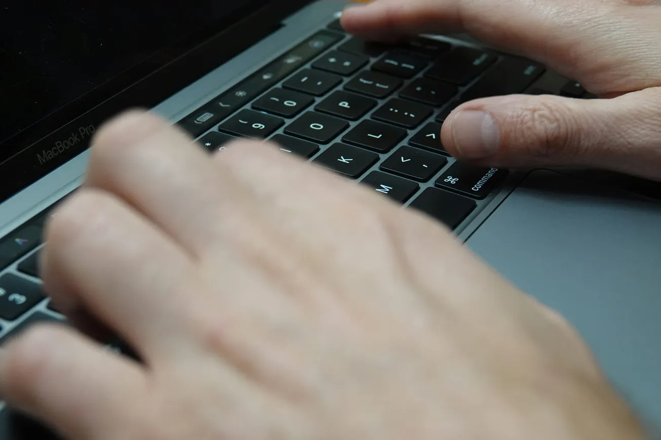 Hands typing on a MacBook keyboard, focusing on the fingers pressing the keys. The image conveys a sense of concentration and productivity.