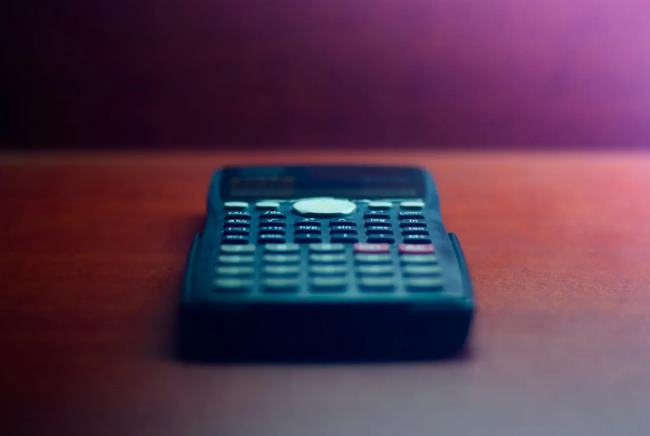 A calculator on a wooden table with a blurred background, bathed in soft, warm light, creating a calm and focused atmosphere.