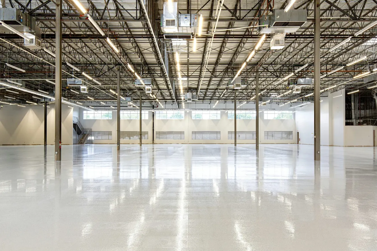 Spacious, bright warehouse with polished floor and grid-patterned ceiling. Large windows and symmetrical pillars create an orderly and modern atmosphere.