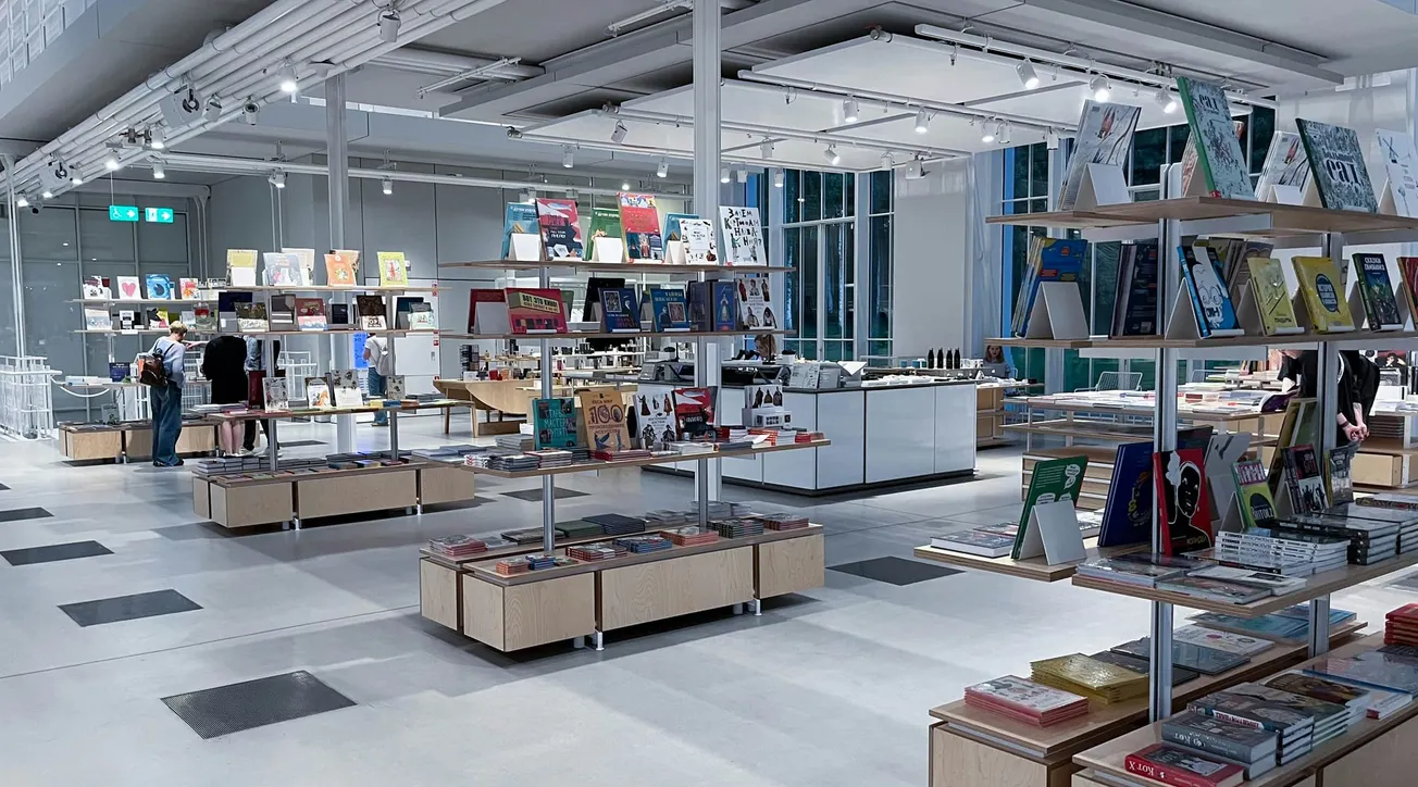 Spacious, modern bookstore interior with bright lighting. Shelves are filled with colorful books and magazines. A few people browse the selection, creating a calm and inviting atmosphere.