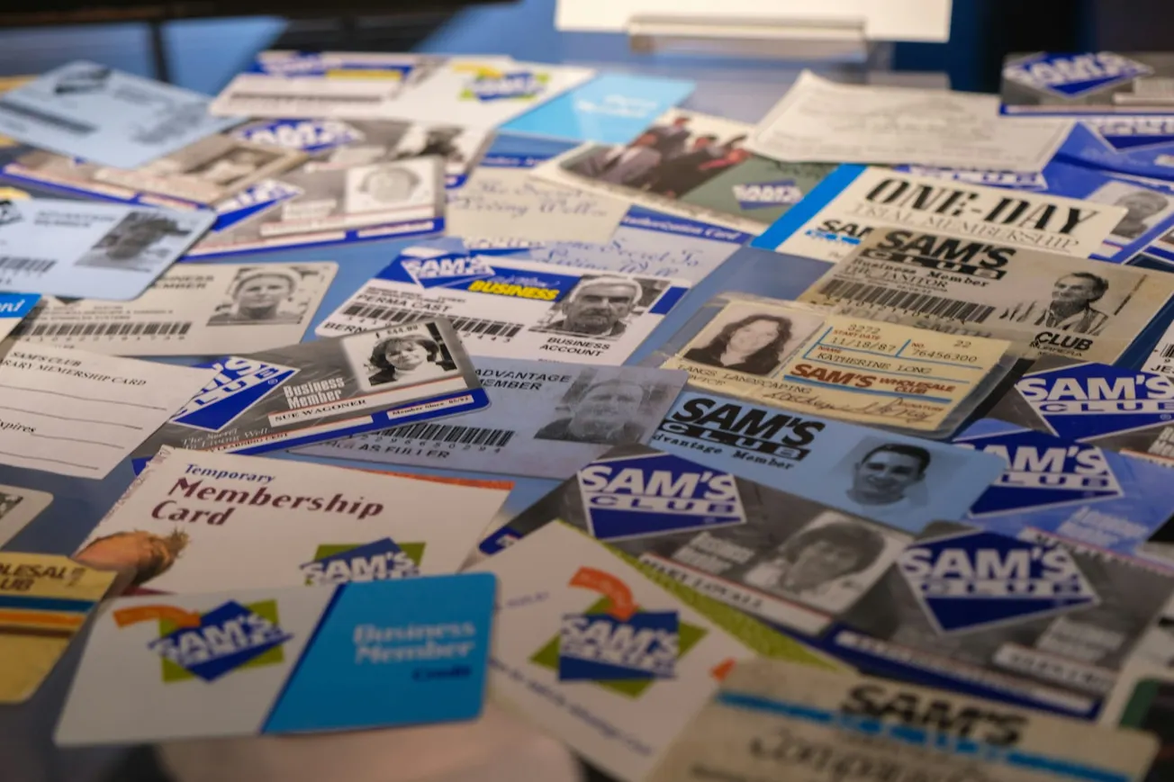 A collection of Sam's Club membership cards are scattered on a surface. The cards, in various designs and colors, display different membership types and photos.