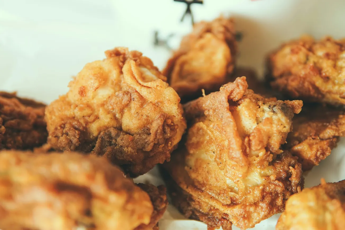 Close-up of several pieces of golden-brown, crispy fried chicken on a white plate. The texture looks crispy, evoking a sense of deliciousness.