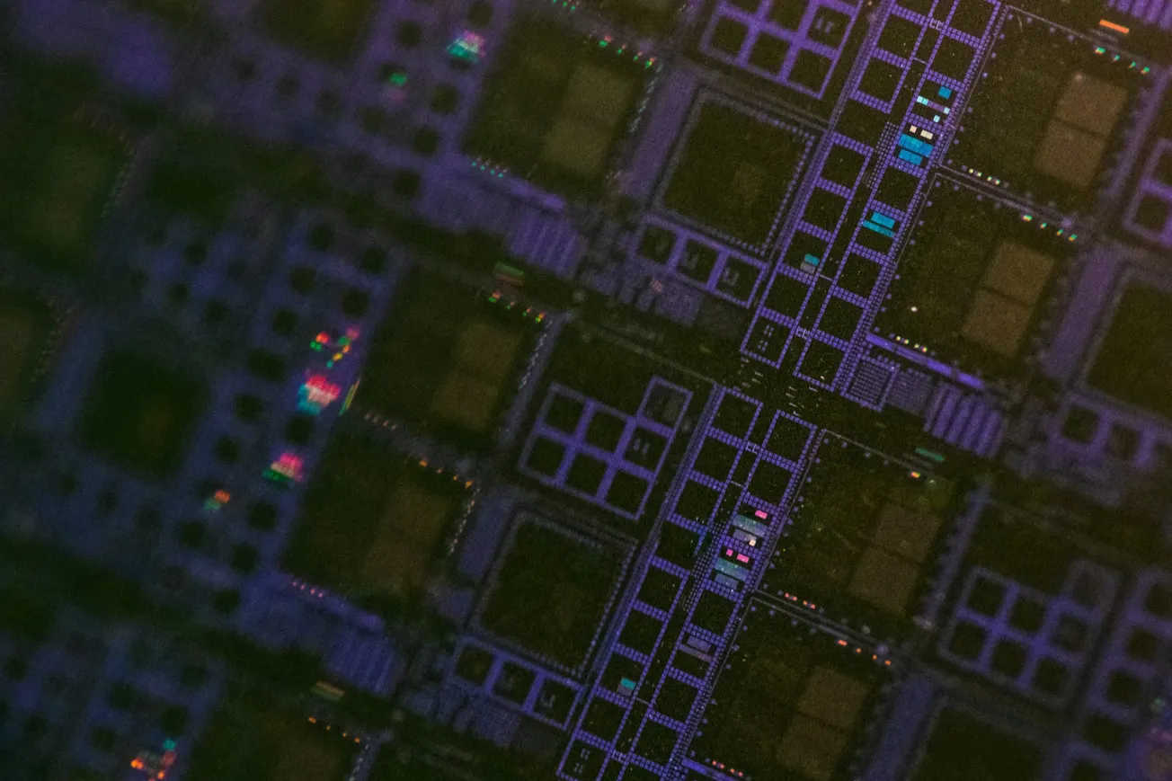 Close-up of a microchip surface showing a grid of intricate, colorful circuits with a dark and iridescent tone, conveying a high-tech feel.