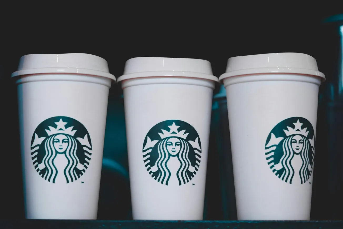 Three white Starbucks coffee cups with green logos are lined up against a dark background, conveying a minimalist and modern vibe.