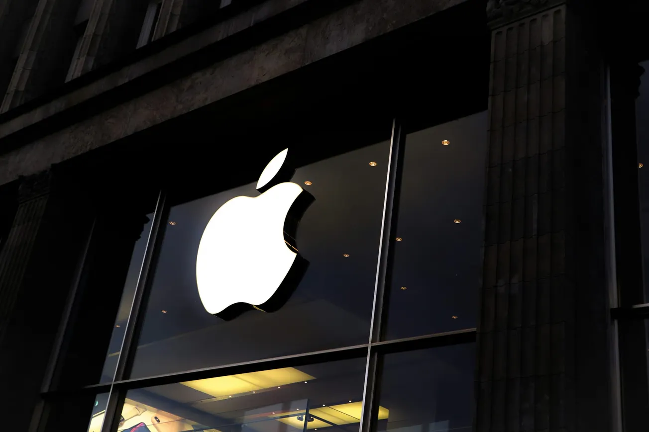 Brightly lit Apple logo on a storefront window, in a dim urban setting, exuding a sleek and modern ambiance, enticing technology enthusiasts.