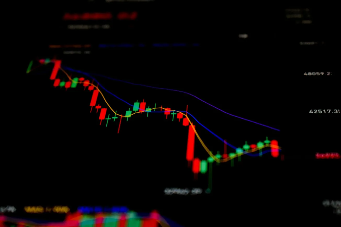 Close-up of a digital financial chart displaying red and green candlesticks, with blue and yellow trend lines on a black background, indicating market trends.