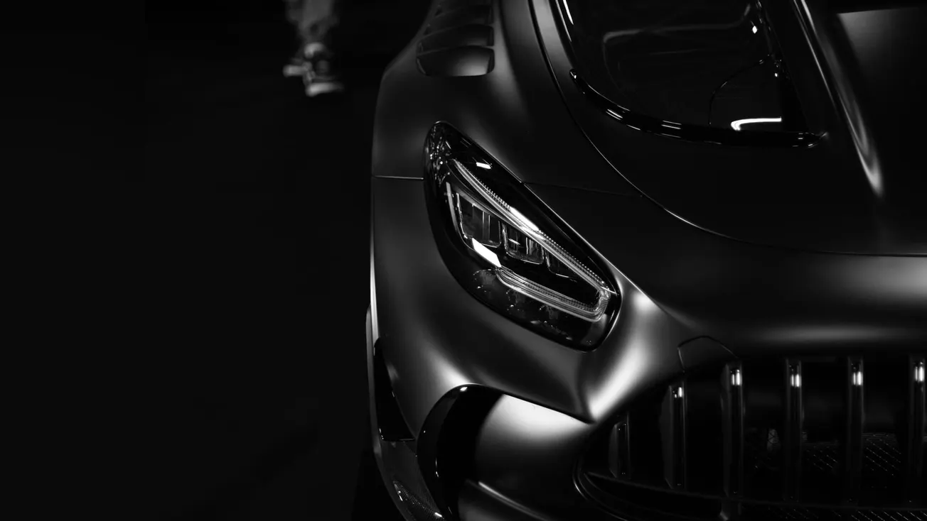 Close-up of a sleek, luxury sports car's front in black and white. The glossy finish and sharp headlight convey a modern, sophisticated feel.